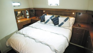 The owner's cabin features a full-sized double berth with easy access from both sides, and plenty of clothes storage. The photo shows a teak interior