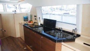 A galley unit, built in the same walnut as the floor, with high-gloss Corian worktop. The hob and sink may be covered when not in use, and behind the doors are a fridge, electric oven and storage