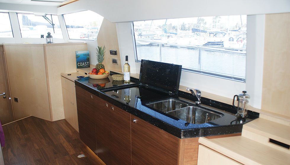 A galley unit, built in the same walnut as the floor, with high-gloss Corian worktop. The hob and sink may be covered when not in use, and behind the doors are a fridge, electric oven and storage